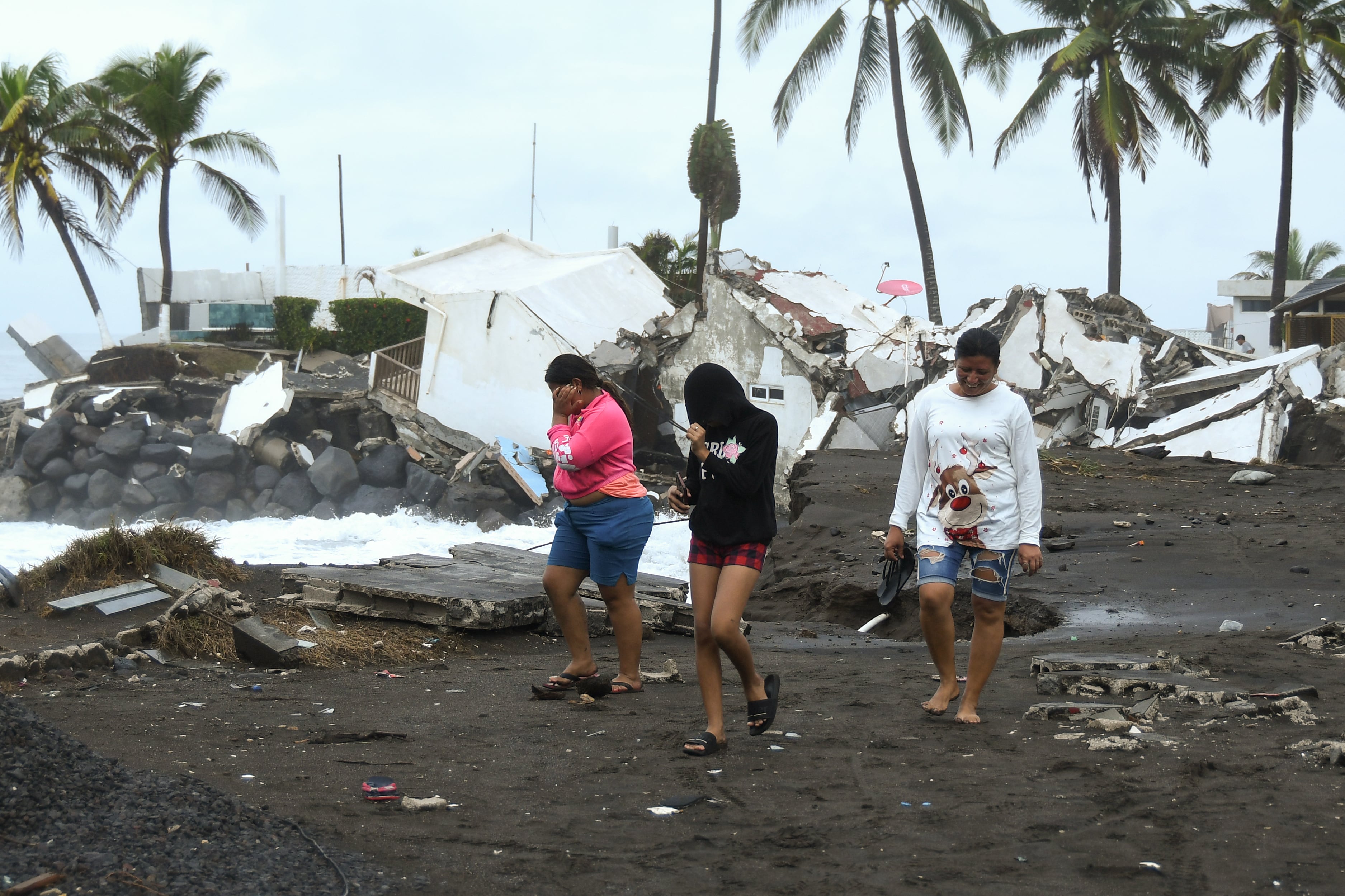 AME444. IZTAPA (GUATEMALA), 10/06/2026.- Personas caminan cerca de viviendas destruidas debido al fuerte oleaje y constantes lluvias generadas por la tormenta tropical Cristina este miércoles en el puerto de Iztapa (Guatemala). Guatemala tiene más de 800 puntos de riesgo a deslaves e inundaciones, entre otros, según cálculos oficiales. EFE/ Alex Cruz