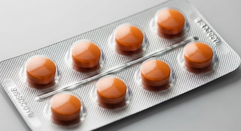 Un blíster plateado contiene ocho comprimidos redondos de color anaranjado, dispuestos en dos filas sobre un fondo claro. Se aprecian detalles de textura.