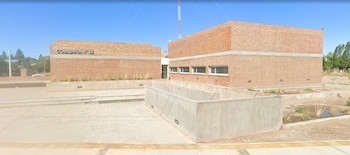 Edificio de ladrillo visto con el texto Comisaría N° 52 en la pared, rampas y muros de hormigón en un día despejado