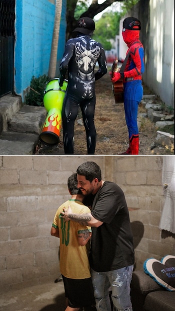 Dos personas disfrazadas de Venom con un tambor y Spider-Man con una guitarra, junto a dos hombres abrazándose, uno con camiseta amarilla y otro negra