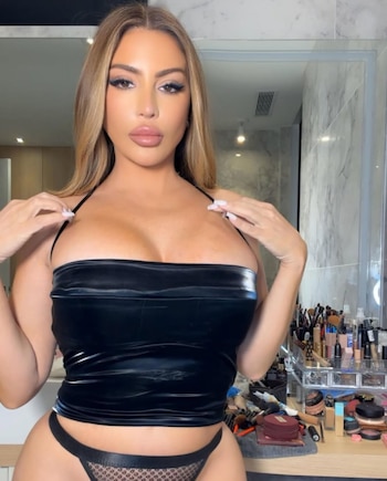 Larsa Pippen, con cabello rubio largo y labios prominentes, posa con un top bandeau negro y una braguita de encaje. Hay productos de maquillaje a su derecha