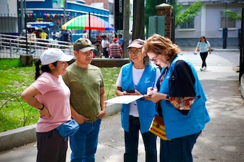 Cuatro personas conversan en la acera; dos de ellas visten chalecos azules con la inscripción Poder Ciudadano y toman notas en papel