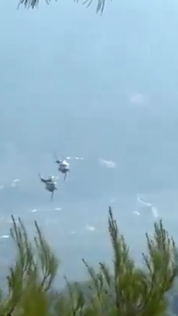 Dos helicópteros en el aire, uno detrás del otro, con hojas de árboles borrosas en la parte inferior y superior de la imagen