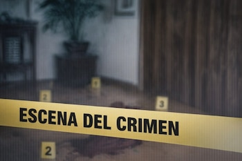 Una cinta amarilla con la frase "Escena del crimen" cruzada en primer plano, con manchas oscuras y marcadores numerados en el suelo.