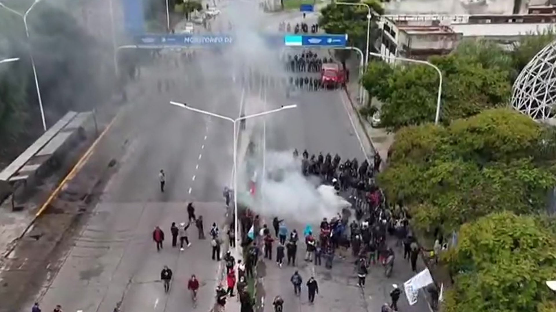 Una vista aérea muestra el momento de tensión durante una protesta en Avellaneda, donde manifestantes y fuerzas de seguridad se enfrentan en la calle con presencia de humo. (Captura de video)