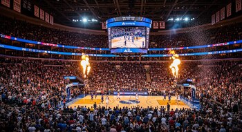 Vista aérea de un estadio de baloncesto de la NBA lleno de gente, con el partido en progreso, un marcador gigante, llamas de pirotecnia y confeti.