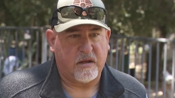 Primer plano de Roger Schultz, un hombre con gorra beige, gafas de sol en la gorra, barba de chivo gris y chaqueta oscura