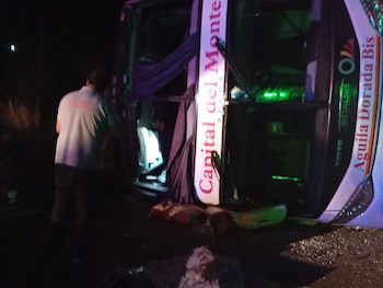 Autobús volcado de color blanco, rojo y verde, con textos Capital del Monte y Águila Dorada. Una persona de espaldas está junto al autobús