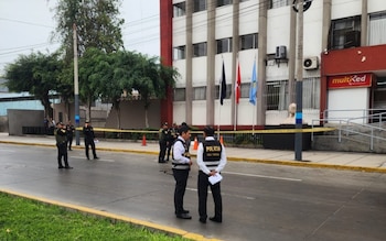 Varios efectivos policiales permanecen en una calle acordonada con cinta amarilla frente a un edificio institucional con banderas