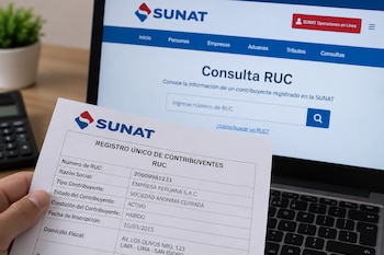 Una mano sostiene una hoja con datos del RUC frente a una computadora portátil que muestra el portal web de la SUNAT