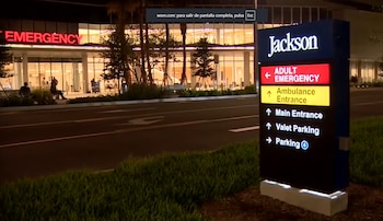 Un letrero luminoso de Jackson con indicaciones para la entrada de urgencias de adultos frente al edificio del hospital iluminado de noche