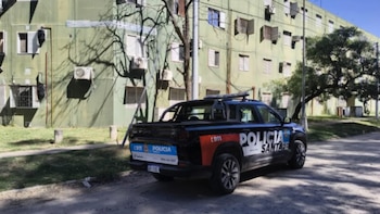 Camioneta de la Policía de Santa Fe estacionada frente a un edificio de apartamentos verde claro con múltiples ventanas y unidades de aire acondicionado