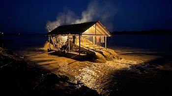 Una draga de madera iluminada en un río por la noche vierte agua en la corriente mientras sale vapor de su interior.