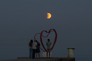 Beach-goers stand a shore of the Black Sea with a full moon also known as "Blood Moon" during a phase of a total eclipse in the background in Odesa, on September 7, 2025, amid the Russian invasion of Ukraine. Stargazers will have a chance to see a "Blood Moon" on September 7, 2025, night during a total lunar eclipse visible across Asia and swathes of Europe and Africa. (Photo by Oleksandr GIMANOV / AFP)