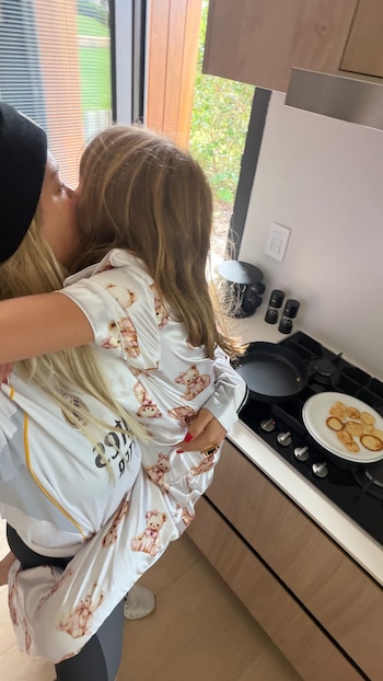 Wanda Nara, con gorro negro, abraza y besa a una de sus hijas, quien viste pijamas de ositos, en una cocina con una estufa y tortitas en un plato