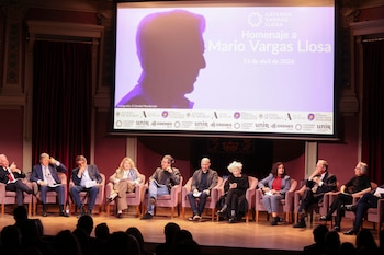 Un panel de diez personas sentadas en un escenario frente a un público, con una gran pantalla de proyección mostrando la silueta de Mario Vargas Llosa
