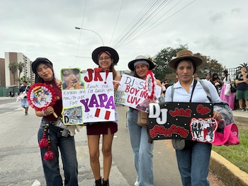 Cuatro mujeres con sombreros sostienen carteles decorados con pancartas y fotografías del grupo BTS en la vía pública