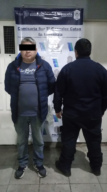 Dos hombres de pie frente a un cartel de la Comisaría Sur 2° González Catán en La Matanza. Uno viste chaqueta azul y jeans, el otro está de espaldas