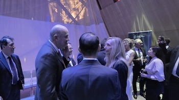 Varias personas con traje conversan en un recinto frente a un panel de la Embajada de la República Argentina en Francia