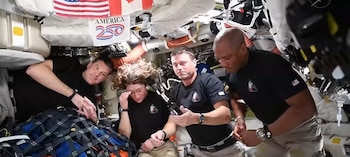 Cuatro astronautas, tres hombres y una mujer con el pelo flotando, manipulan equipaje y objetos sueltos dentro del módulo de una estación espacial