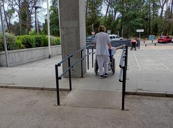 Una celadora transporta a un paciente onclógico por fuera del hospital para entrar por otro acceso a la unidad de radioterapia