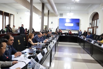 Numerosas personas en una sala de reuniones del Congreso de la República con una mesa larga, sillas, documentos, micrófonos y una gran pantalla