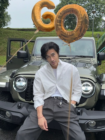 Un hombre con camisa blanca posa apoyado en un todoterreno verde con dos globos dorados que forman el número 60
