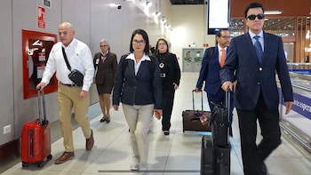 Varias personas con vestimenta formal caminan por el pasillo de un aeropuerto y llevan maletas con ruedas