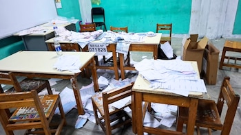 Mesas y sillas escolares con abundantes hojas de papel y actas electorales desordenadas sobre los tableros y esparcidas por el suelo