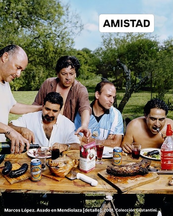 Cinco hombres en una mesa de madera. Hay chorizos, carne, cabeza de cerdo, botellas de vino, latas de cerveza, vasos. Fondo de árboles. Cartel blanco con ‘AMISTAD’