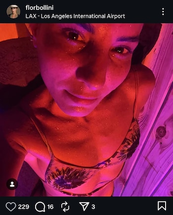 Selfie de una mujer con piel brillante por sudor o agua, iluminada con luz roja y morada, vistiendo un bikini de patrón oscuro, mirando a cámara