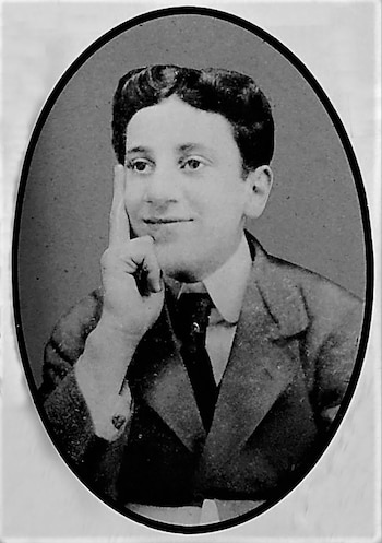 Retrato en blanco y negro de un joven con cabello oscuro peinado hacia atrás, traje y corbata, con el dedo índice izquierdo tocando su barbilla y una leve sonrisa. La imagen es ovalada