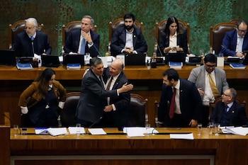 Diputados chilenos en una sesión parlamentaria, con dos hombres de traje abrazándose en el centro, rodeados de otros legisladores sentados en escritorios de madera