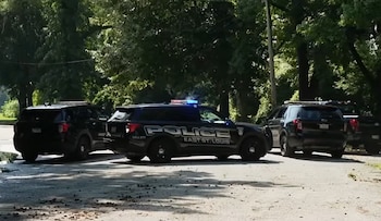Tres vehículos SUV de la policía de East St. Louis en una calle de tierra. Uno tiene luces azules y rojas encendidas. Árboles al fondo