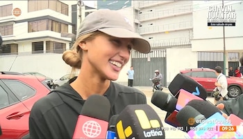 Alessia Rovegno, con gorra gris y cabello recogido en un moño, sonríe ampliamente mientras varios micrófonos se acercan para entrevistarla