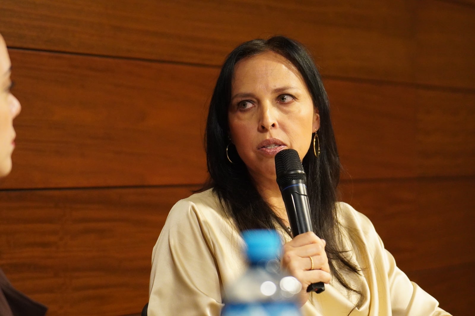 Una mujer sostiene un micrófono y habla ante la audiencia durante una conferencia en un salón con pared de madera. (Durante años, Elena Molina Vivanco buscó una respuesta para síntomas que no encontraban nombre en ningún diagnóstico: migrañas, fatiga, problemas digestivos e intolerancias alimentarias que se acumulaban sin que los análisis clínicos ofrecieran una explicación. Esa búsqueda, larga e incierta, se convirtió en el punto de partida de El grito silencioso del cuerpo, su primer libro, publicado con Editorial Planeta Perú, con el que la comunicadora busca visibilizar en el país la histaminosis por déficit de DAO, una condición médica que puede permanecer sin identificar durante años en personas con síntomas persistentes.)