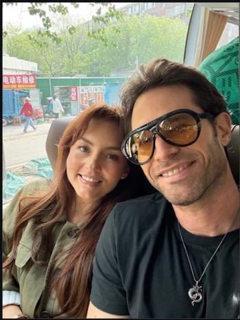 Selfie de Angelique Boyer y Sebastián Rulli sonriendo, con ella a la izquierda y él a la derecha usando gafas de sol, dentro de un vehículo