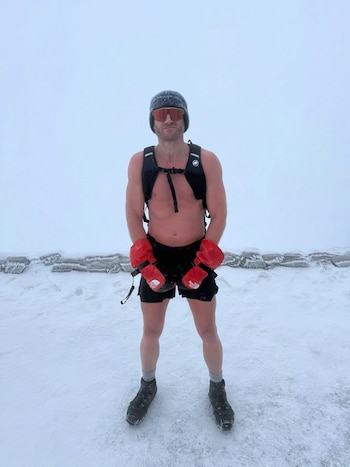 Primer plano de un hombre con barba, André Schurrle, usando una linterna frontal que ilumina su rostro sobre un fondo oscuro, lleva una camiseta roja
