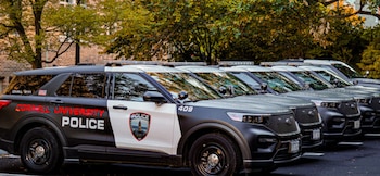 Una hilera de vehículos policiales negros con la inscripción Cornell University Police estacionados frente a un edificio de ladrillos
