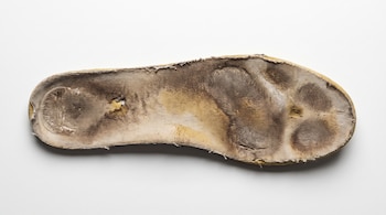 Plantilla de zapato deportivo gastada con manchas oscuras y amarillentas, compresión en talón y metatarso, textura ligeramente húmeda, sobre superficie blanca.