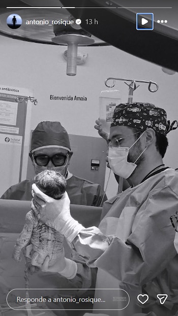 Fotografía en blanco y negro de Antonio Rosique en un quirófano, sosteniendo a su hija recién nacida, Amaia. Otro médico observa cerca