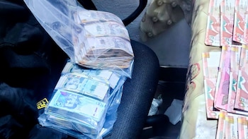 Fajos de billetes peruanos en bolsas de plástico sobre una silla de oficina y billetes alineados sobre una mesa