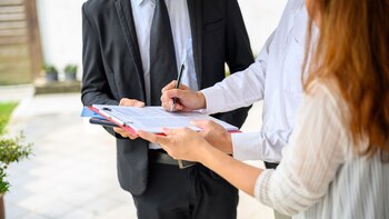 Couple signing contract agreement with digital tablet from real estate agent in front of their new house. Concept for real estate, moving home or renting property.