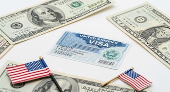 Visto americano sobre fundo branco com notas de 100 e 20 dólares e duas pequenas bandeiras americanas.