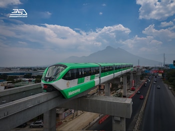 Tren monorriel verde y blanco de Metrorrey en vía elevada. Debajo, carretera con tráfico y edificios, con montañas y cielo nublado de fondo