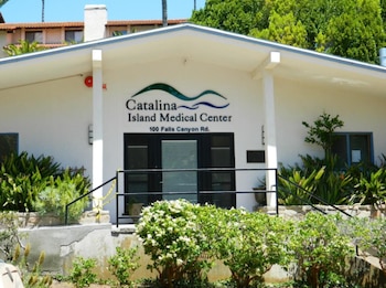 Fachada blanca del Centro Médico Isla Catalina con su letrero, la dirección 100 Falls Canyon Road, una puerta doble y vegetación