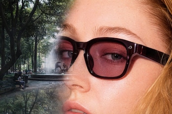Un rostro con ojos, nariz y boca, gafas de sol oscuras de lentes rojizos. Detrás, un parque con árboles, fuente de piedra, agua, bancos y personas.
