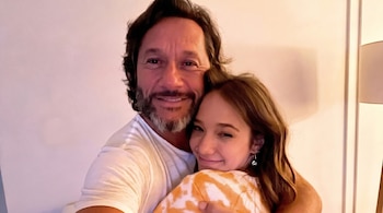 Diego Torres, un hombre de cabello oscuro y barba canosa, abraza sonriente a Ángela Torres, una mujer joven con cabello castaño y sonrisa sutil