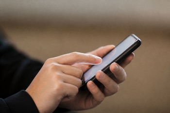 Primer plano de dos manos que sostienen y tocan la pantalla de un teléfono inteligente negro.