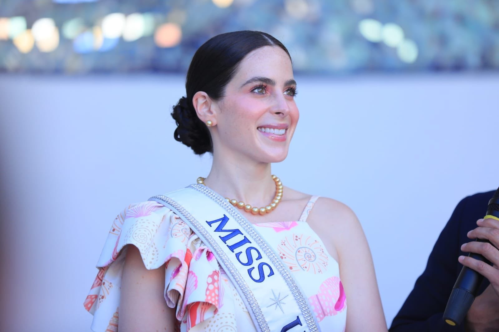 Una participante del concurso Miss Universo sonríe con gracia, luciendo un vestido estampado, un collar de perlas y su banda de Miss U. (Alcalde de La Libertad Sur, Henry Flores)